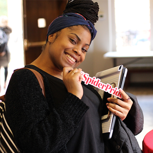 Smiling student holding up a sticker that says #SpiderPride.
